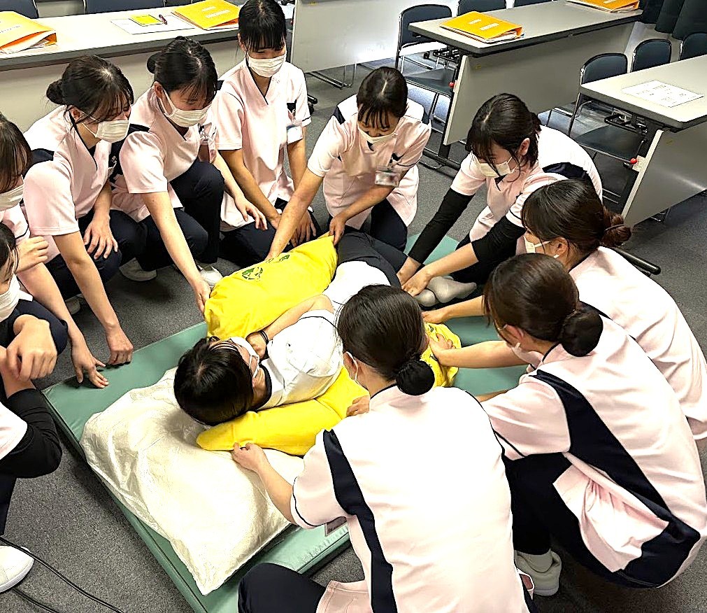 写真：人物模型をベッドに横たえて、作業について説明を受けている様子